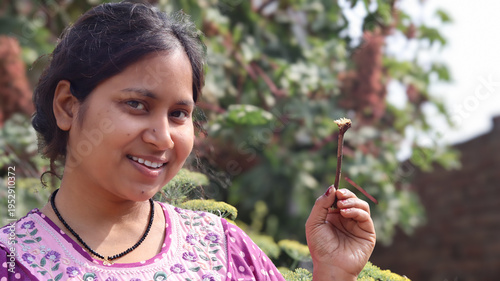 Bild auf Leinwand ​A happy young South Asian woman smiling while holding an Acacia (Babool) twig, demonstrating a traditional and eco-friendly way of oral hygiene in a green garden