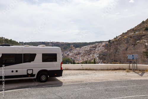White camper van parked on a road overlooking a cliffside village in Spain