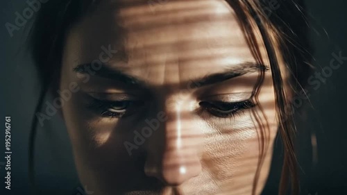 Close-up portrait of a woman with downcast eyes and shadows on her face.