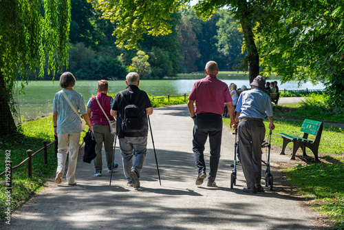 Zwei ältere Männer, und andere Senioren gehen entspannt im Park spazieren -  Sohn und Opa mit Rollator