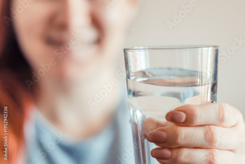 Woman holding glass of clean water in her hands. Portrait of a young smiling red-haired woman. World Water Day.