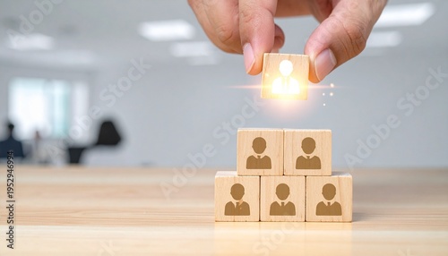 Conceptual Leadership and Target Marketing Image of a Person's Hand Placing a Glowing Target Icon Block at the Peak of a Pyramid Made of Wooden Blocks with Human Silhouettes