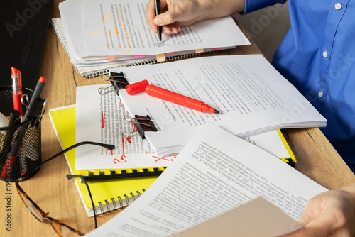 Cuadro en lienzo Professional editor reviews and marks up printed documents surrounded by stacks of papers, notebooks, and writing tools