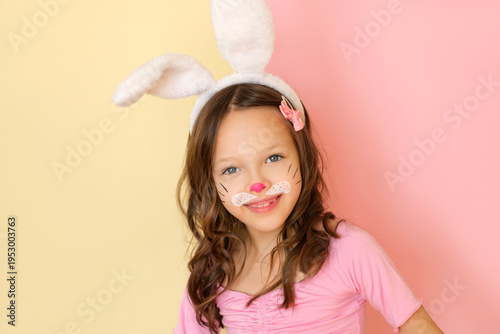 A playful funny girl with a painted face and rabbit ears looks cheerfully at the camera, rejoicing at the approach of the Easter holiday.