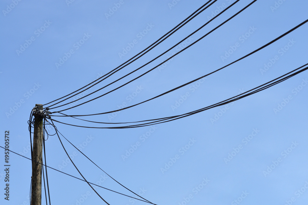 Fototapeta premium A weathered wooden utility pole stands against a clear blue sky with several black power lines stretching across the frame