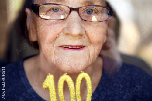 Portrait of an elderly woman with glasses holding anniversary candles.  An old woman holds a birthday cake alone on her centenary.