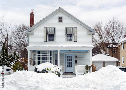 Traditional white New England house stands behind massive snowbanks after a winter storm in Greater Boston area, Massachusetts