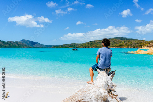 Man sitting on driftwood enjoying stunning Whitehaven Beach, Australia
