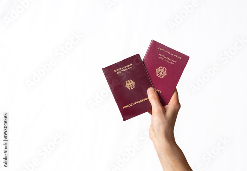 Person's hand holding two burgundy German passports against a clean white background with passport and documents