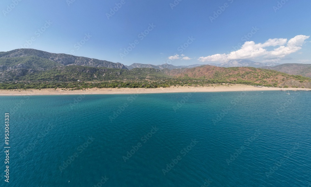 Fototapeta premium Aerial view of a stunning Mediterranean coastline featuring crystal clear turquoise waters - pristine sandy beach - and dramatic mountainous landscape under blue sky