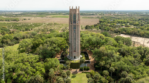 A sweeping drone shot captures the iconic Bok Tower surrounded by greenery and scenic countryside in Central Florida.