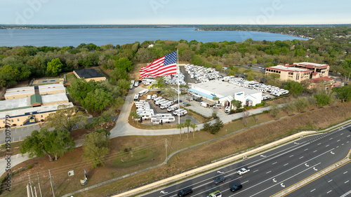 A large American flag waves prominently above Highway 27 in Clermont, Florida, captured from a sweeping aerial drone perspective.
