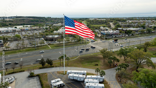 A cinematic drone view showcases a towering American flag overlooking a busy intersection along Highway 27 in Clermont, Florida.
