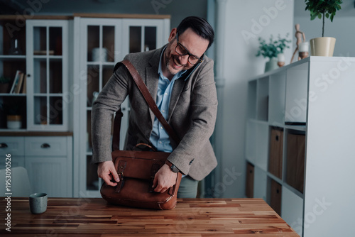 Photos Busy man talking on phone and organizing briefcase, getting ready for work from