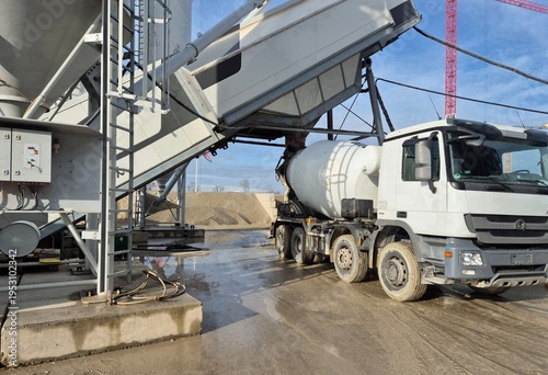 Tableau sur toile A professional front-side view of a heavy-duty concrete mixer truck positioned under a mobile batching plant