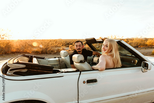 Couple sitting in convertible car looking back