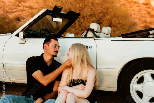 affectionate couple sitting by car in the desert