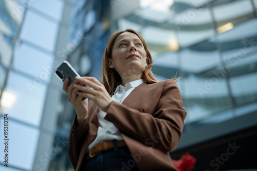 Professional woman holding smartphone looking up at city