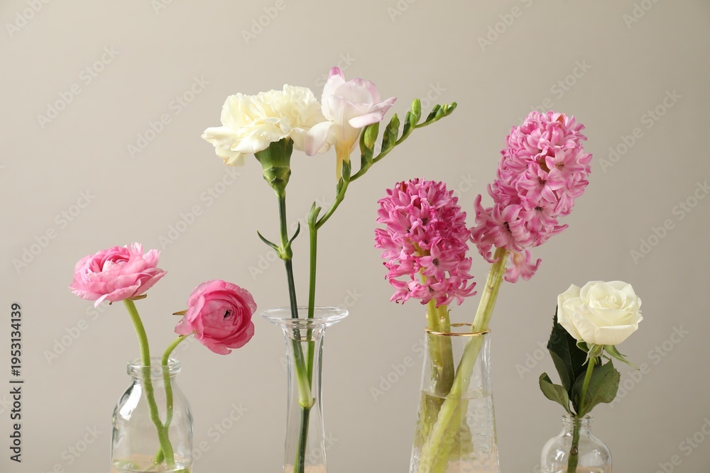 Obraz premium Beautiful flowers in vases against light background, closeup