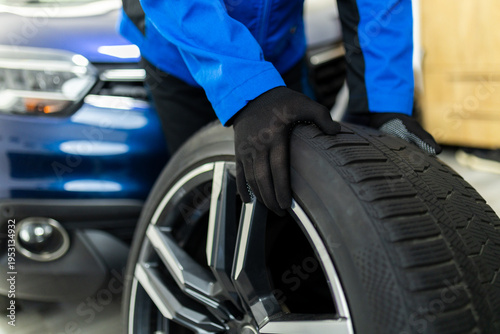 Bild auf Leinwand Mechanic holding car wheel tire during replacement in auto workshop