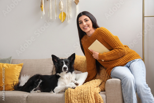 Young woman with book and cute Border Collie dog on sofa at home