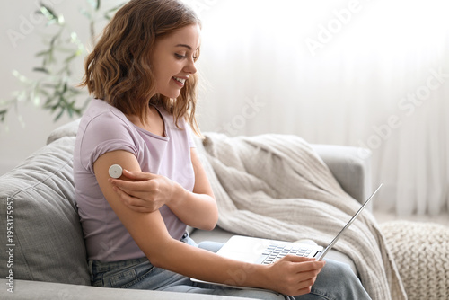 Diabetic young woman with glucose sensor talking to doctor online on sofa at ...