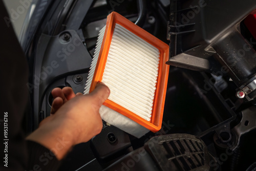 Mechanic removing orange-framed air filter from engine bay during replacement service in auto repair shop