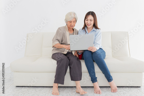 Asian female and old female search information with laptop computer, they feeling happy and smile, they sitting on sofa, mother's day and happiness family time, technology and social network.