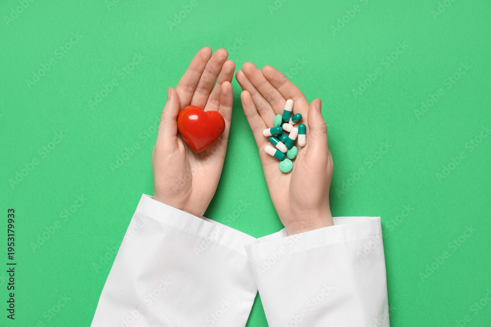 Fototapeta premium Female doctor's hands with red heart and different pills on green background