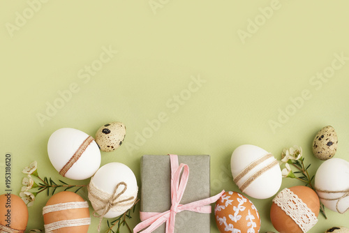 Composition with decorated Easter eggs, present and small flowers on green background