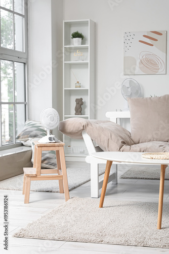 Interior of light living room with couch and electric fan on stepladder