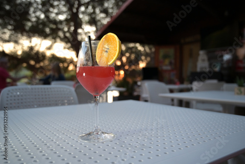 cocktail alcolico rosso in un bicchiere con una fetta d'arancia servito in una pineta vicino al mare in una sera d'estate