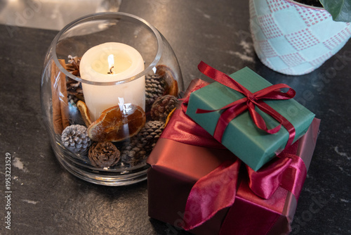 Glass bowl holding lit pillar candle, potpourri on slate tabletop, burgundy and green gifts sitting