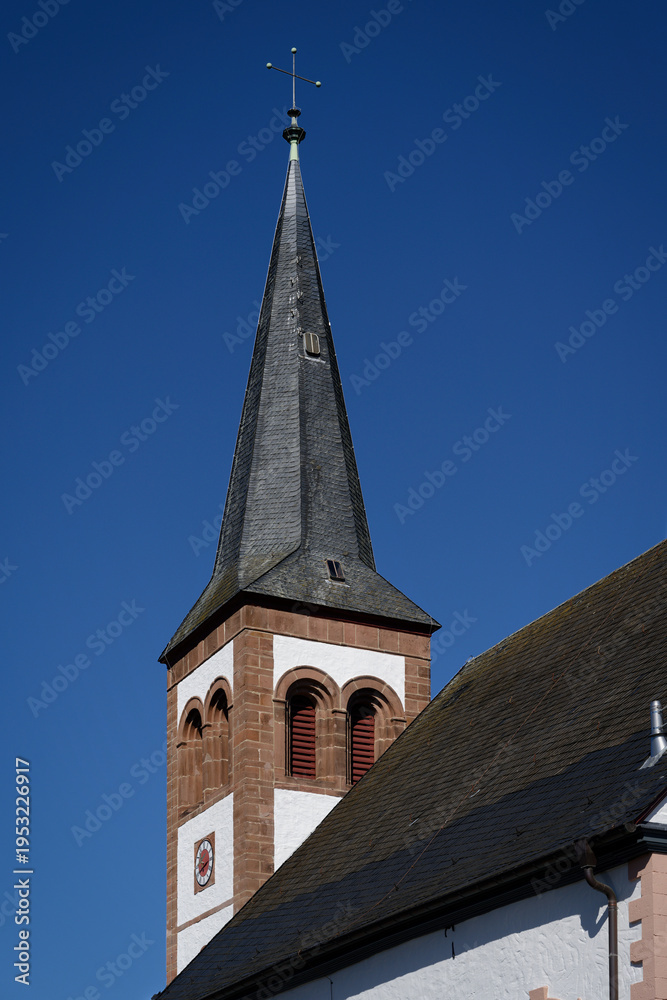 Fototapeta premium Close-up of the historic church tower in Gemünd, Germany. Features a slate roof, sandstone details, and a clear blue sky background.