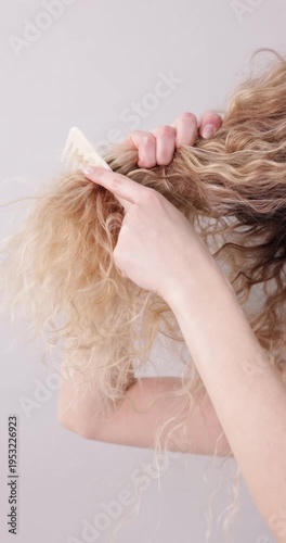 Unhappy woman trying to brush her tangled hair on light grey background