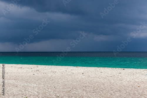 Tropical beach in Koh Adang, Thailand, with clear turquoise water and stormy weather. White sand shoreline under dramatic skies with blue horizon.