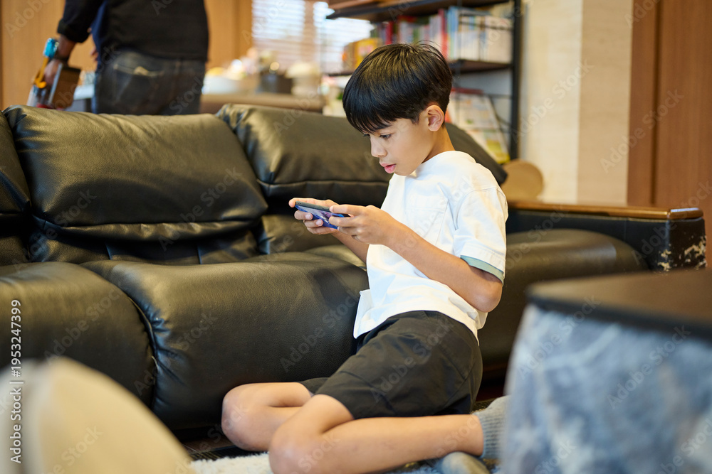 Obraz premium ソファに座りスマホゲームをする男の子