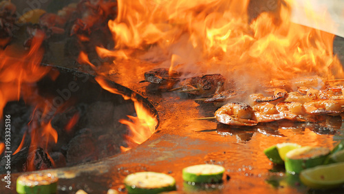 Close-up of shrimp and vegetables cooking on a hot plancha grill with large, dramatic flames. The warm, fiery lighting creates an energetic mood, perfect for food festival or barbecue concepts