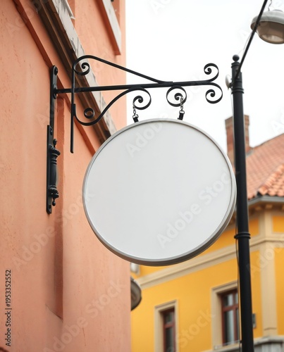 A blank white sign hanging on a black wrought iron bracket outside a building