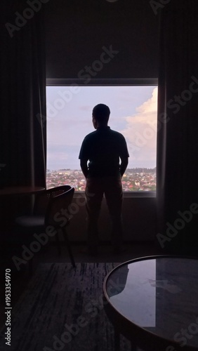 Silhouette of a man looking out the window at sunset