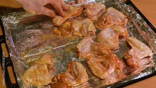 Male hands laying out marinated chicken wings on a baking sheet with foil. The process of preparing dinner, where raw marinated chicken wings are evenly placed on a foil-lined baking sheet for baking