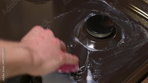 Man cleans boiled over milk from a gas stove using a pink sponge. The process of cleaning a kitchen stove from white foam and spilled milk residues using detergent and a sponge
