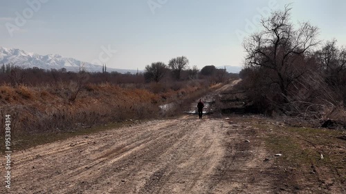 a man goes to a meeting along a dirt rural road, against the background of endless rural open spaces and snow-capped mountains, close-up