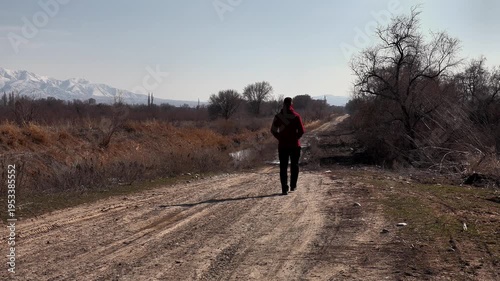 a man walks into the distance along a dirt rural road, against the backdrop of endless rural expanses and snow-capped mountains, close-up