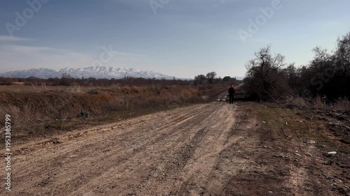 a man goes to a meeting along a dirt rural road, against the background of endless rural expanses and snow-capped mountains