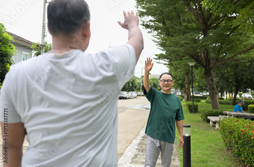 Two senior men greeting each other by raising hands on a neighborhood street before exercise together, showing friendly community interaction