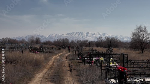 a man walks towards him along a dirt road through an old rural cemetery against the backdrop of graves and mountains in the snow