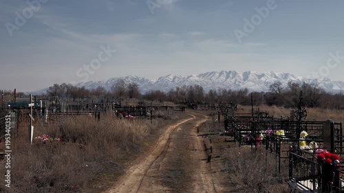 view of an old rural cemetery against the background of mountains in the snow, dirt road, early spring, close-up