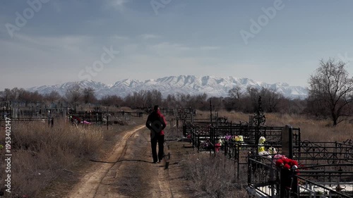 a man walks into the distance along a dirt road through an old rural cemetery against the background of graves and mountains in the snow, close-up
