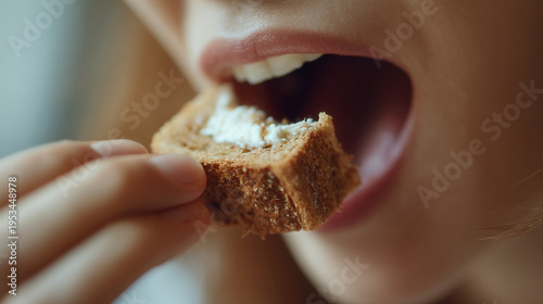 Close-up of a woman eating a piece of whole grain bread with cream cheese